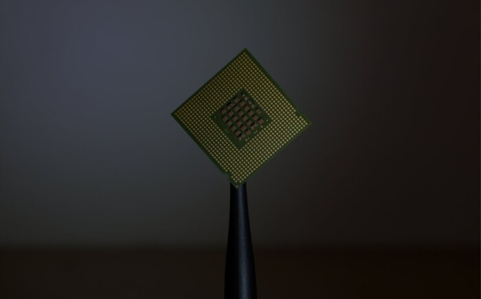 A computer processor chip balanced on the tip of a stylus against a dark background.