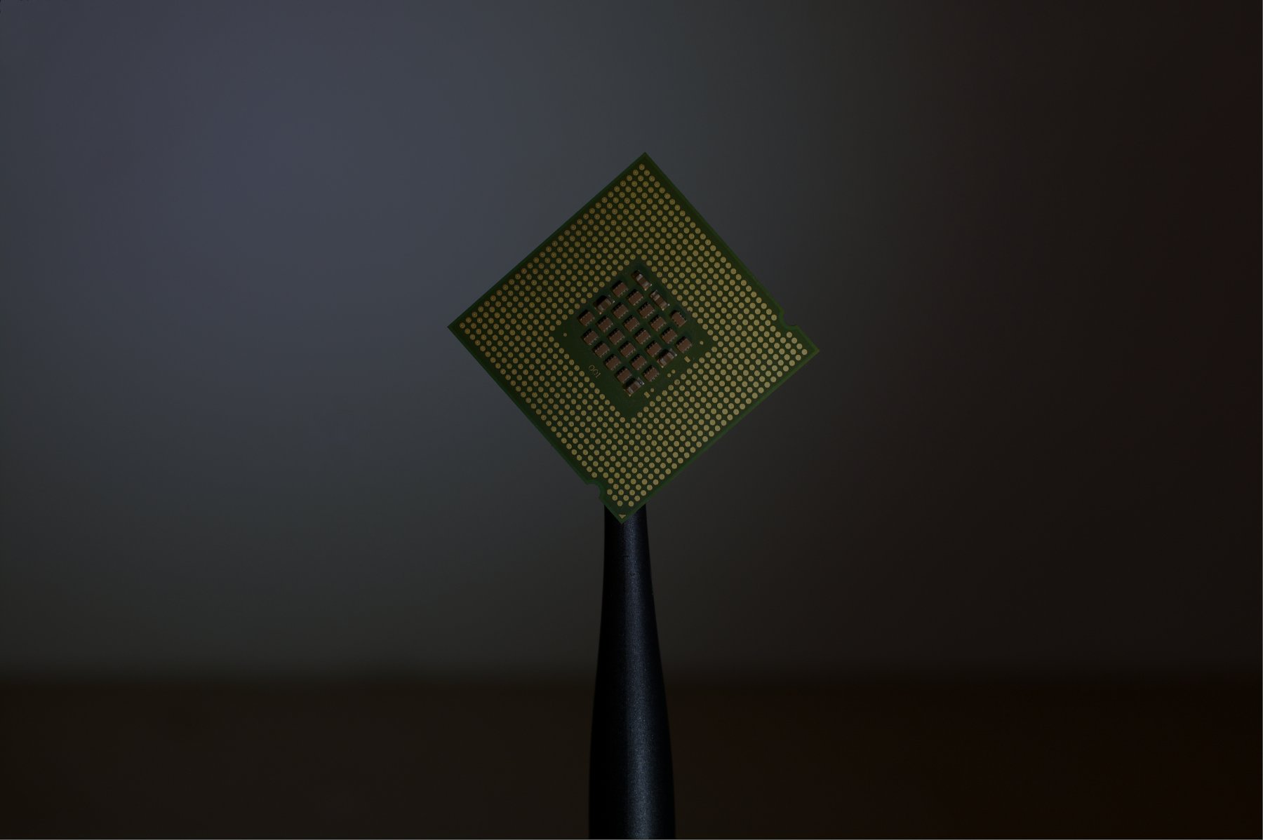 A computer processor chip balanced on the tip of a stylus against a dark background.
