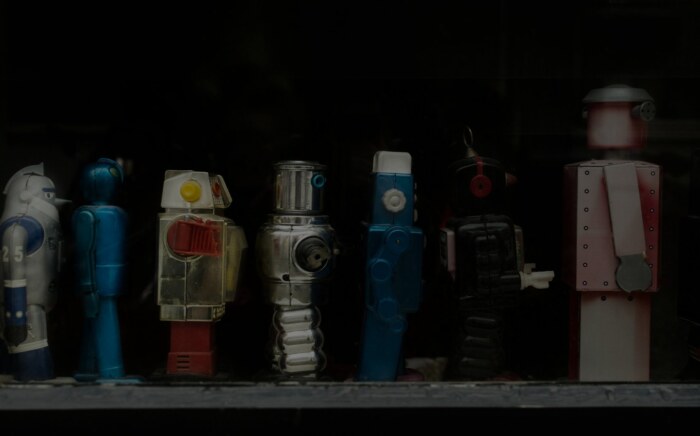A row of vintage tin toy robots lined up in a dark display case.